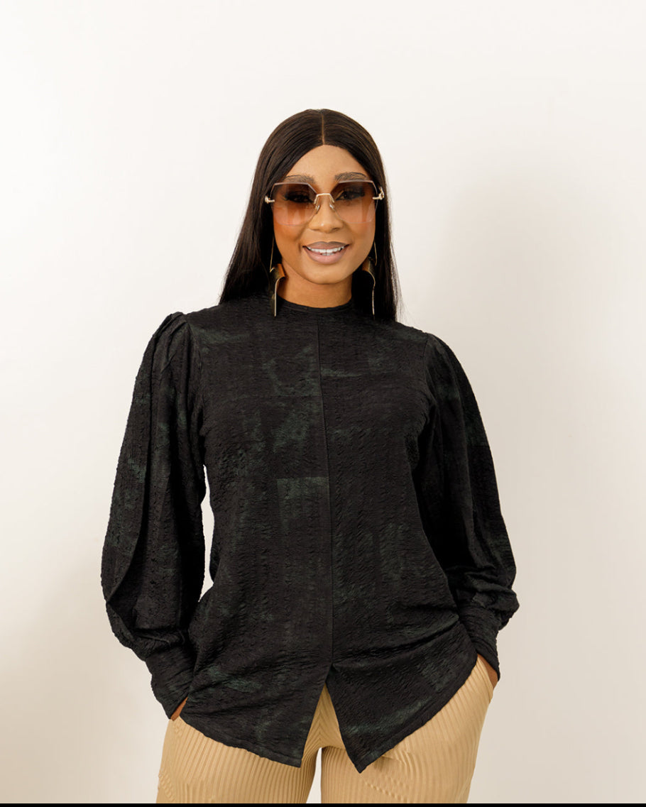 A woman wearing a black and green checkered puffer sleeve top with round neckline, paired with beige trousers and sunglasses.