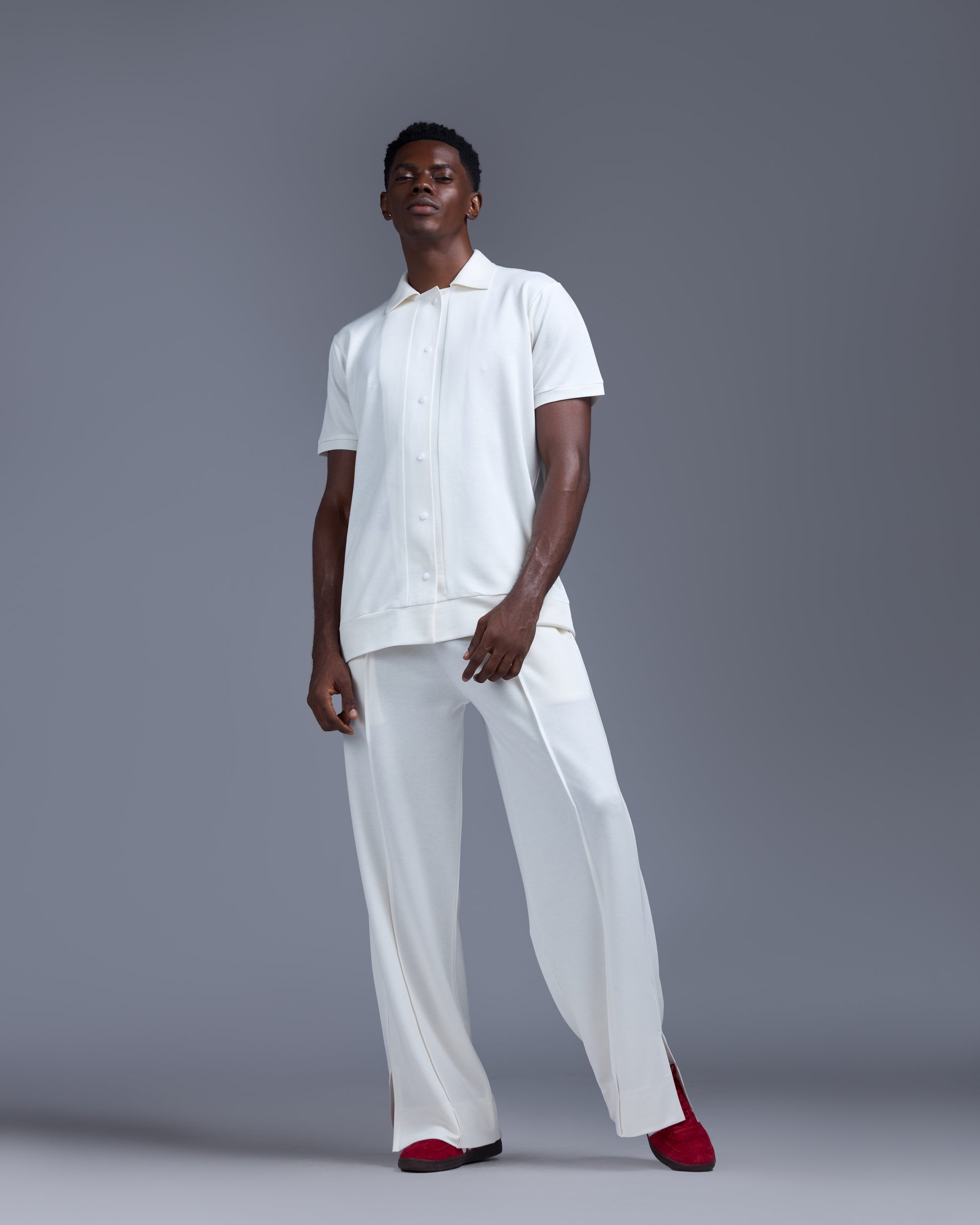 Person wearing a white outfit with red shoes on a gray background