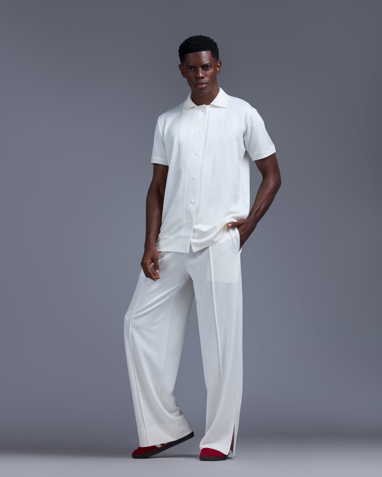 Man wearing a white outfit with red shoes on a gray background