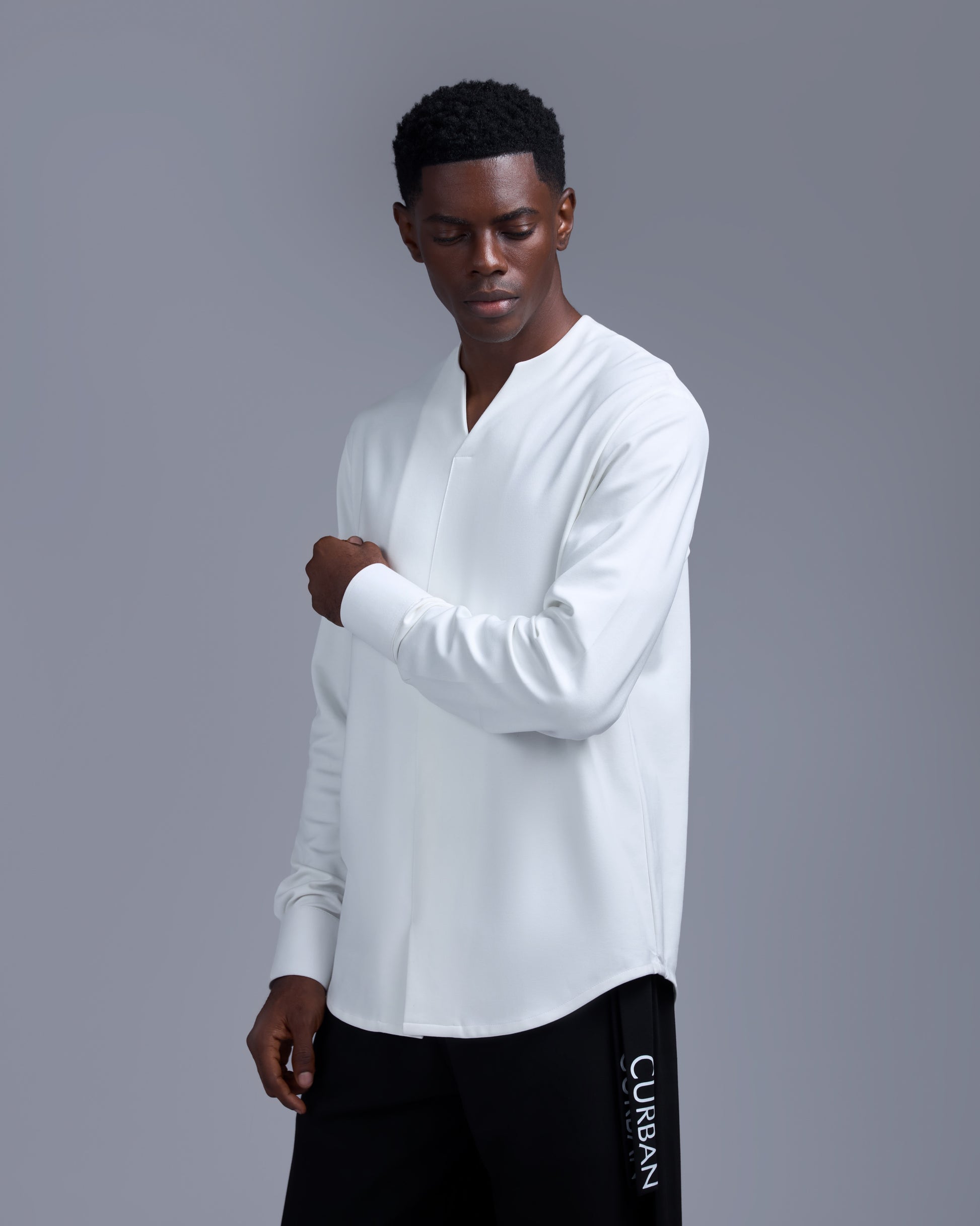 Man wearing a white long-sleeve shirt and black pants with 'Curbank' branding on a gray background
