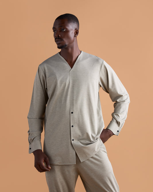 Man wearing a beige long-sleeve shirt and pants against a brown background