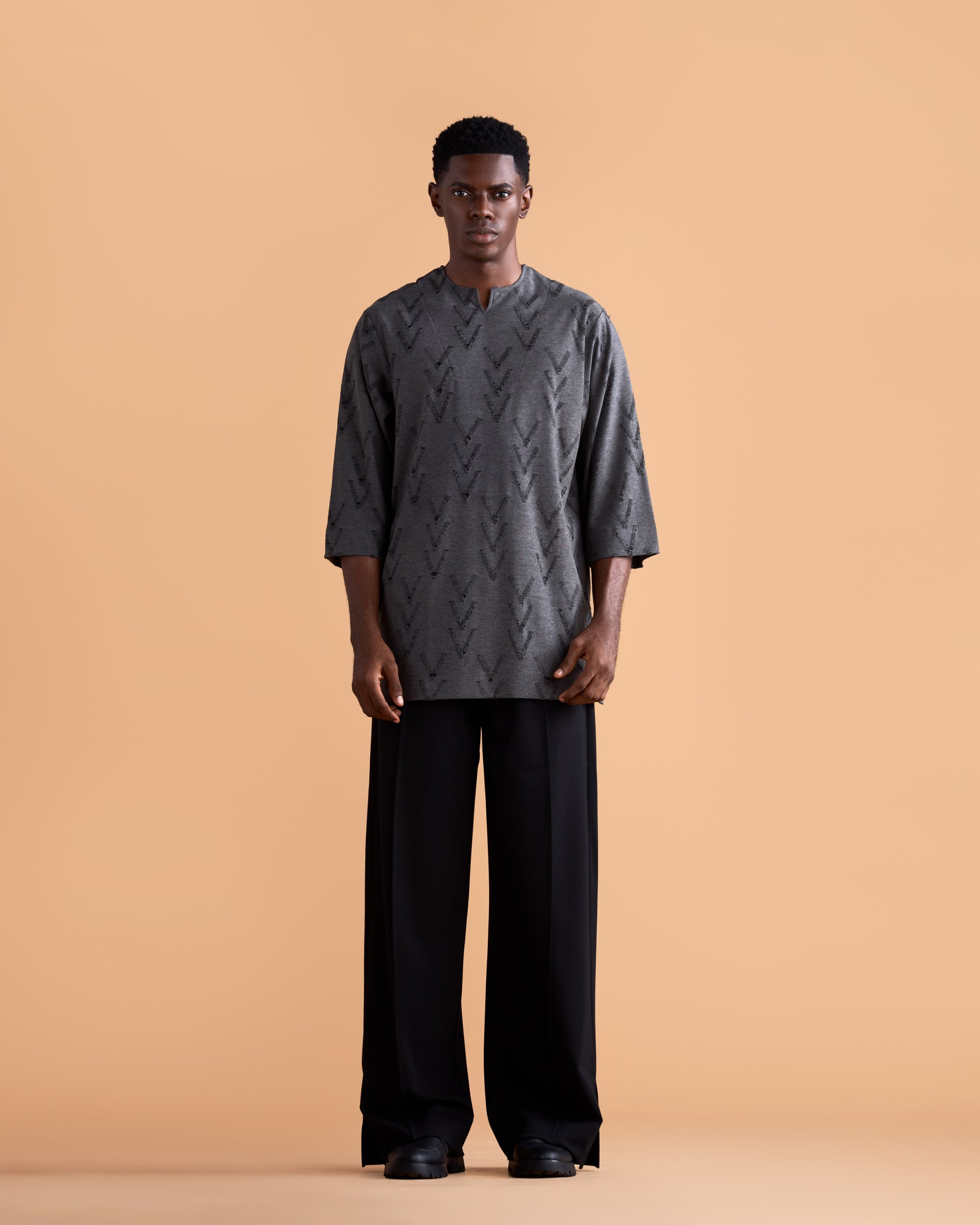 Man wearing a dark gray patterned shirt and black pants on a beige background