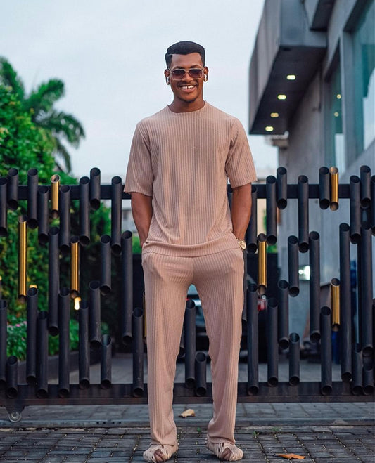 A man standing on stairs wearing a beige oversized t-shirt and matching palazzo pants, both made of cotton, in a pleated texture.